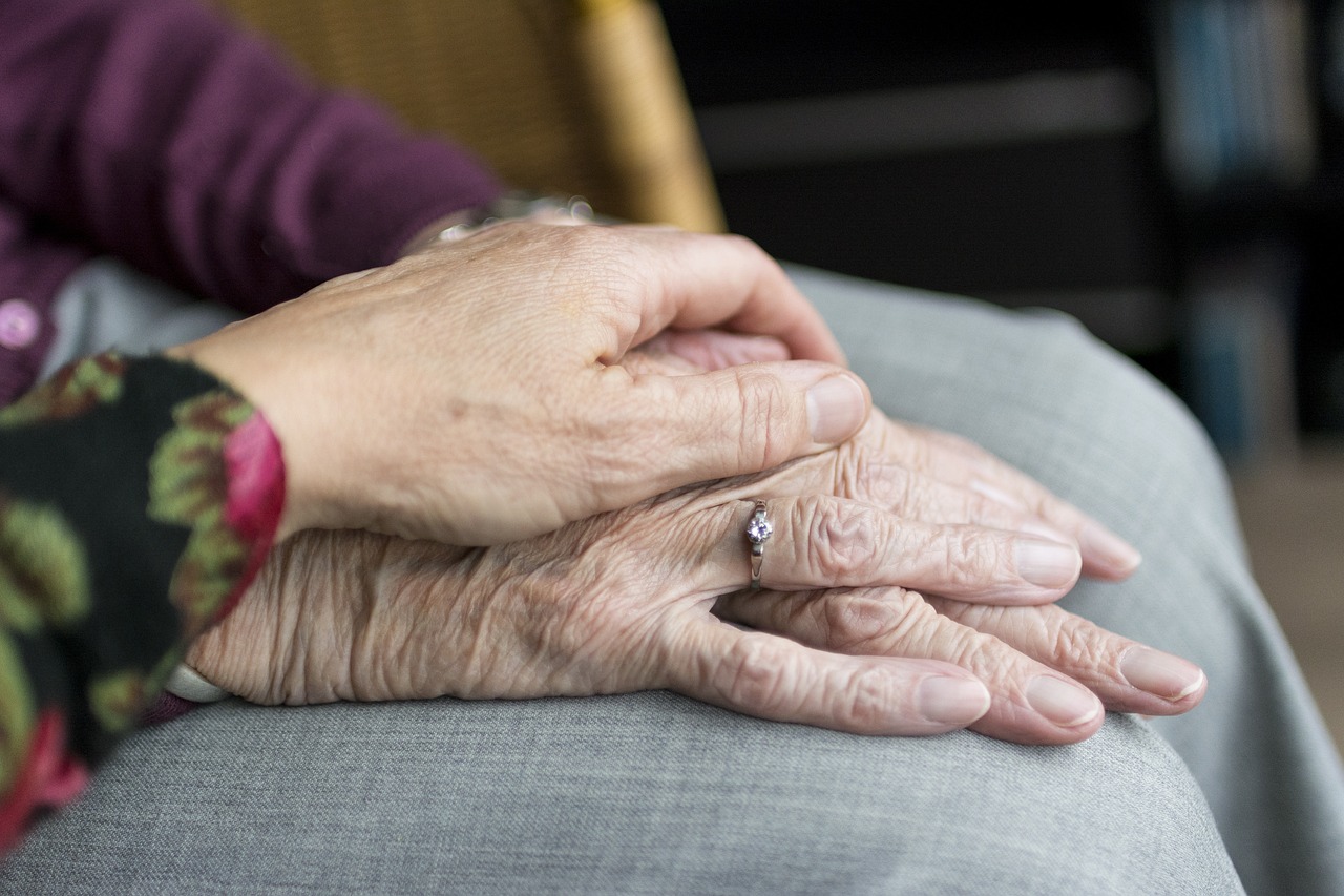 Eine Hand legt sich sanft auf die Hände einer alten Frau